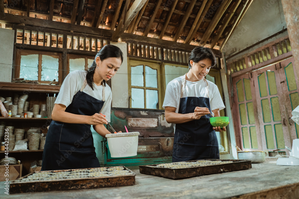 一对穿着围裙的蛋糕制作者正在碗里揉面团，同时在工具箱里烤蛋糕