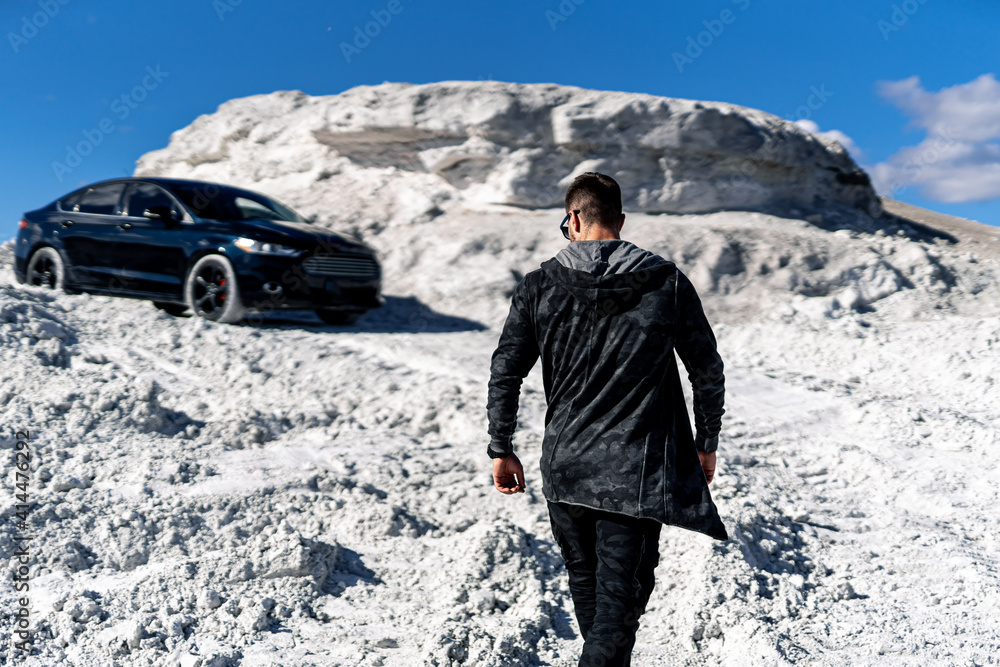 Fashionable young man in cool elegant black coat or jacket. White quarry and luxury black car backgr