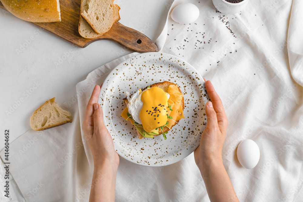 Woman holding plate with tasty sandwich and florentine egg on light background