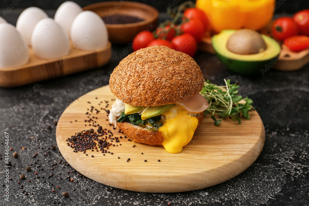 Tasty burger with florentine egg and fresh vegetables on dark background, closeup