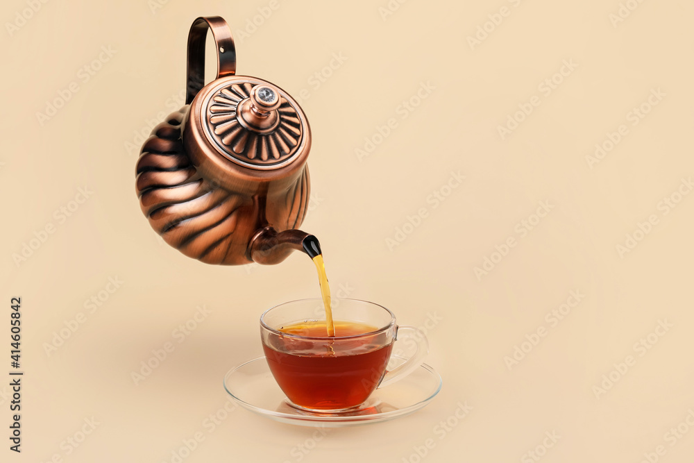 Pouring of hot tea from teapot into cup on color background