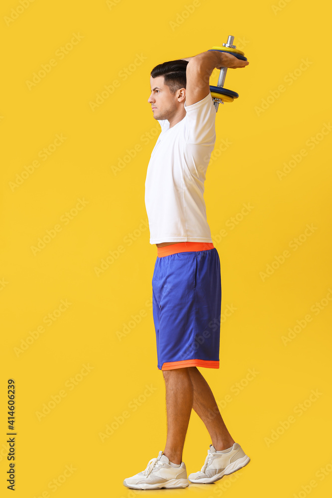 Sporty young man training with dumbbell on color background