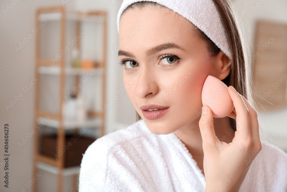 Beautiful young woman with sponge applying makeup at home