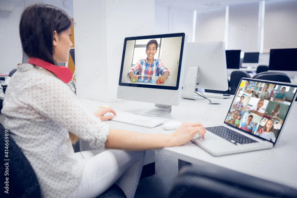 Female teacher wearing headphones having a video call with multiple students at school on laptop and