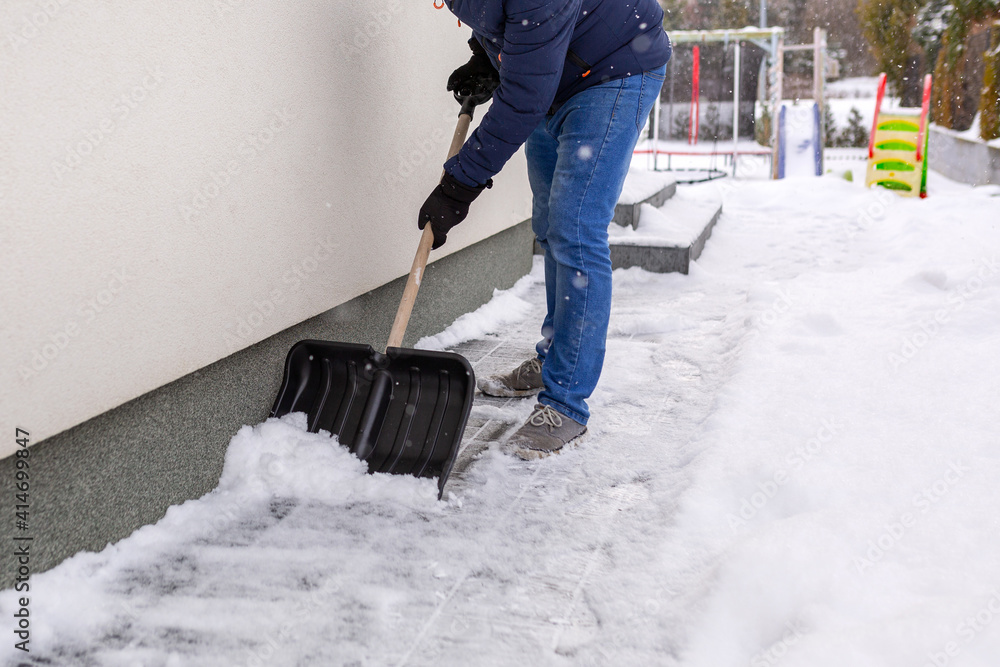 用铲子清除房子前面车道的积雪