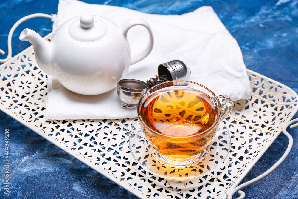 Tray with cup of tea, teapot and dry leaves on color background