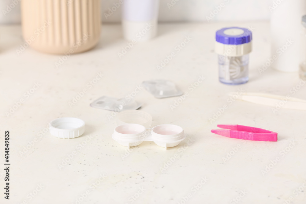 Tweezers and container with contact lenses on light background