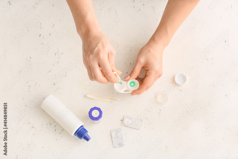 Woman taking contact lens from container on light background