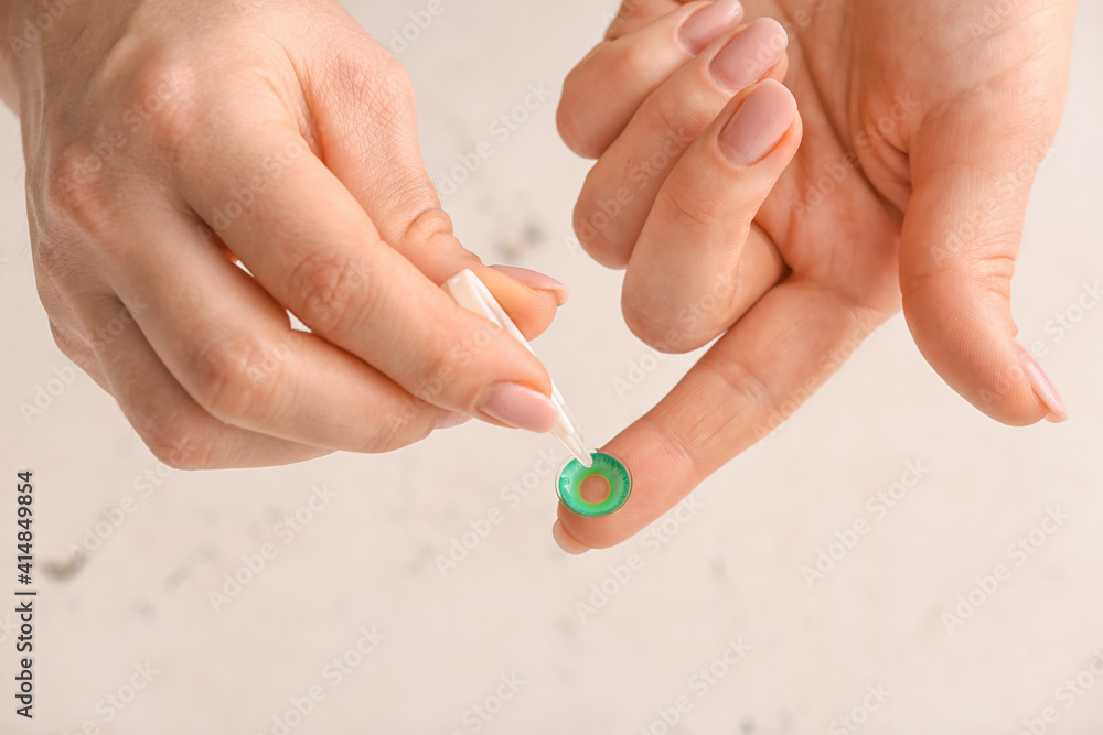 Female hand with tweezers and contact lens on light background