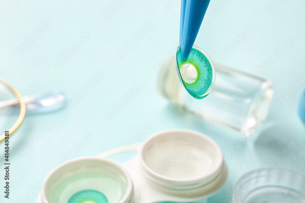 Tweezers with contact lenses on color background