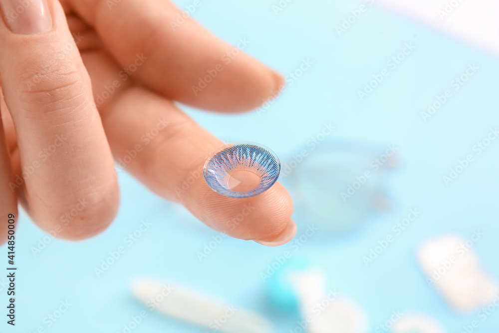 Female hand with contact lens on color background