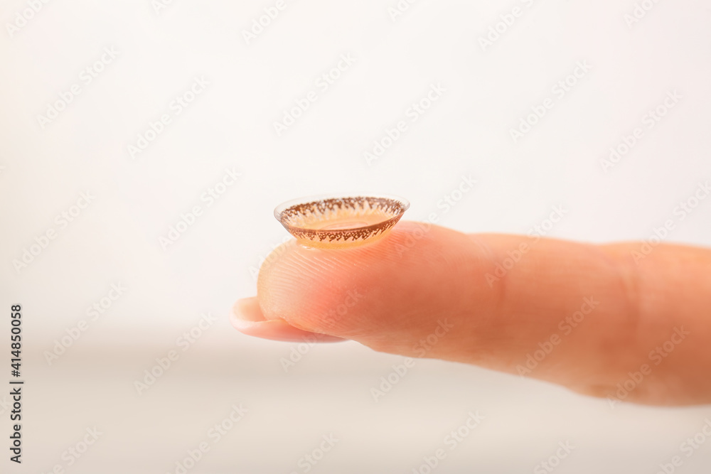 Female finger with contact lens on light background