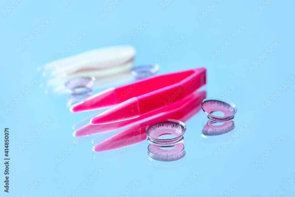 Contact lenses and tweezers on color background