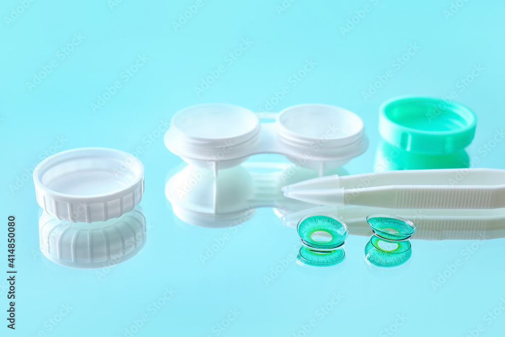 Container with contact lenses and tweezers on color background