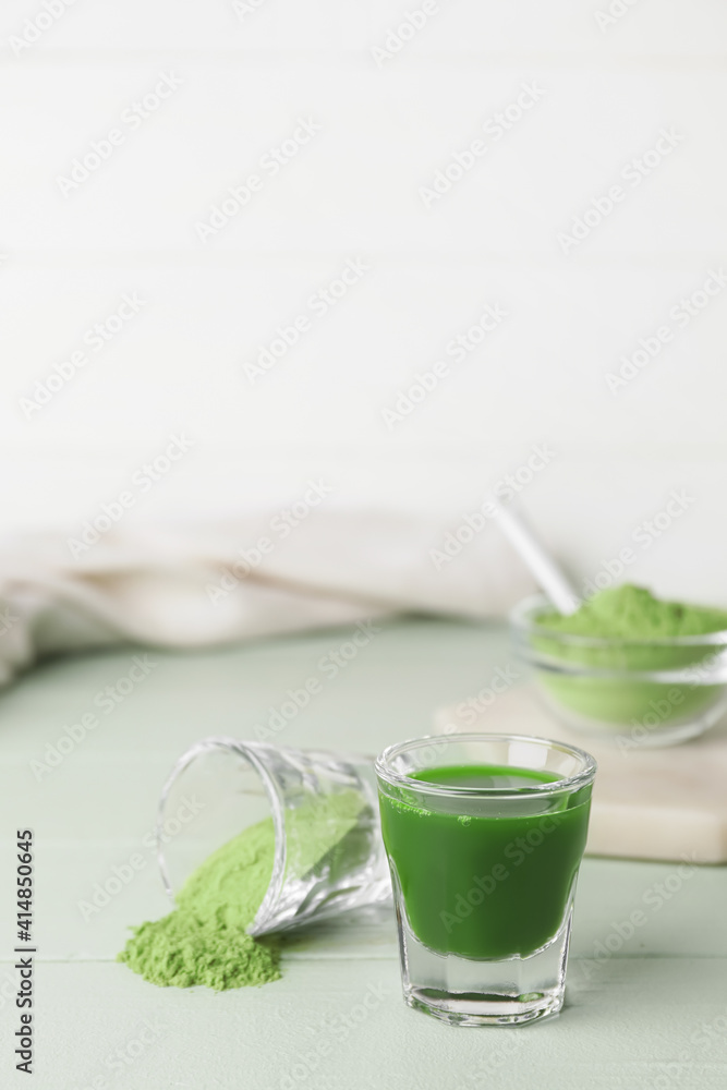 Glass with fresh wheatgrass juice and powder on color wooden background