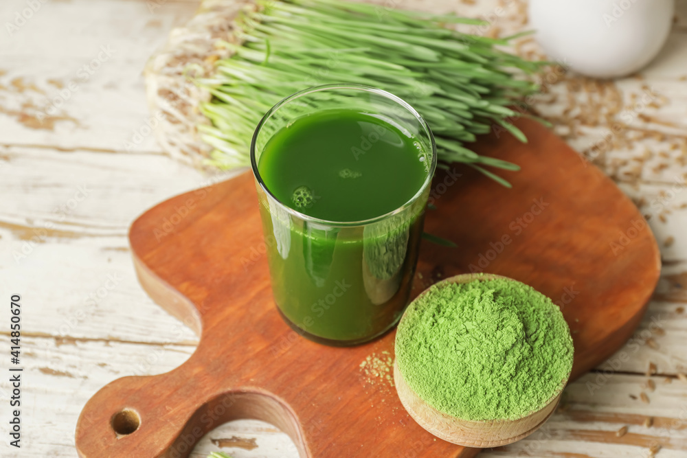 Glass with fresh wheatgrass juice and powder on wooden background