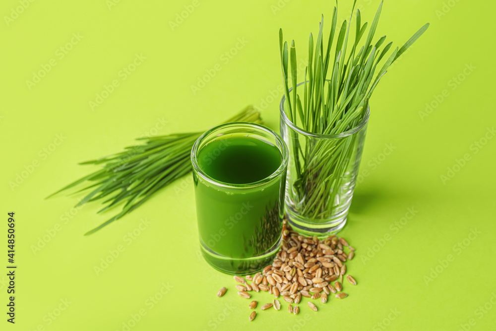 Glass with fresh wheatgrass juice and seeds on color background