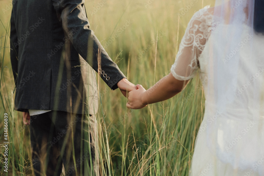 Young Asian couple holding hands and walking in the meadow on a sunny day
