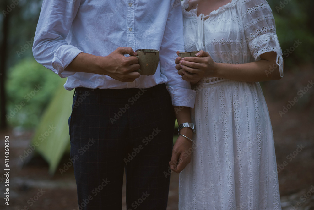 一对年轻的亚洲夫妇晚上在树林里露营时喝咖啡的照片