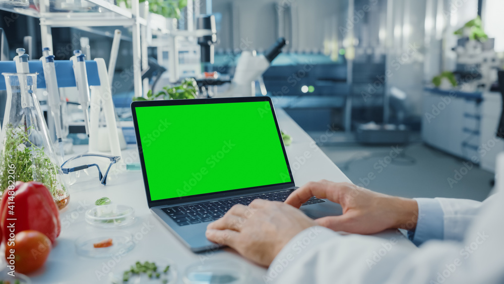 Male Scientist Working on a Laptop Computer with Green Screen Mock Up Display. Microbiologist is at 