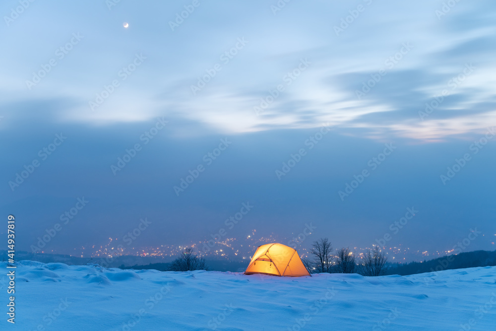 黄色帐篷在雾中城市灯光的背景下从内部点亮。令人惊叹的雪