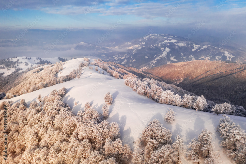 Amazing aerial view of mountains range, meadows and snow-capped peaks in winter time. Forest with fr