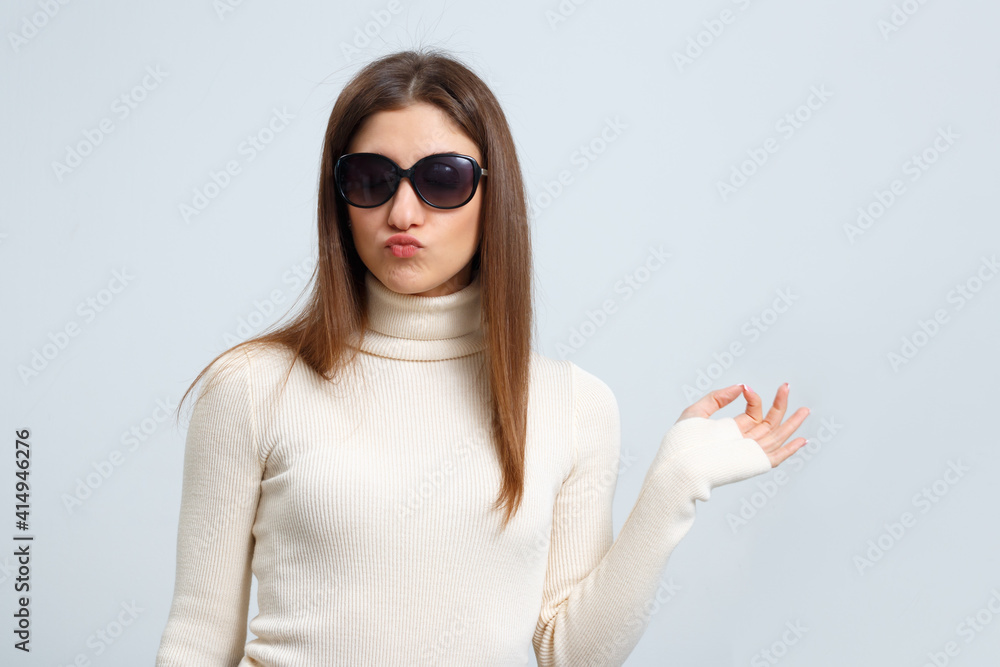 Fashionable girl in sunglasses sends a kiss and shows ok sign on a gray background. Beautiful young 