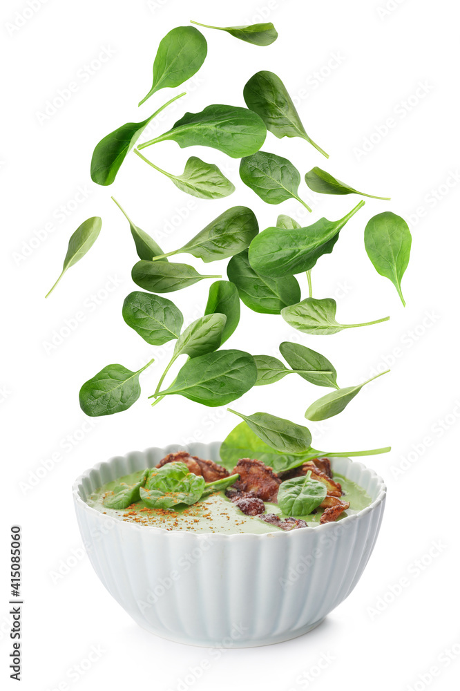 Bowl with tasty soup and falling spinach leaves on white background