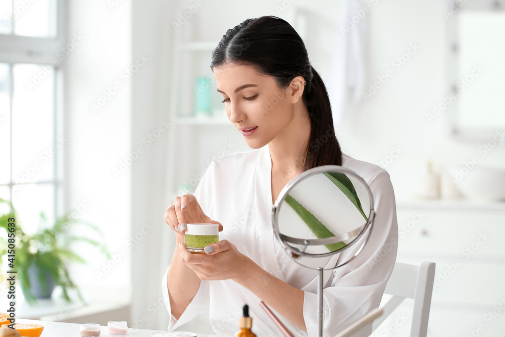 Beautiful young woman with cosmetic product in bathroom