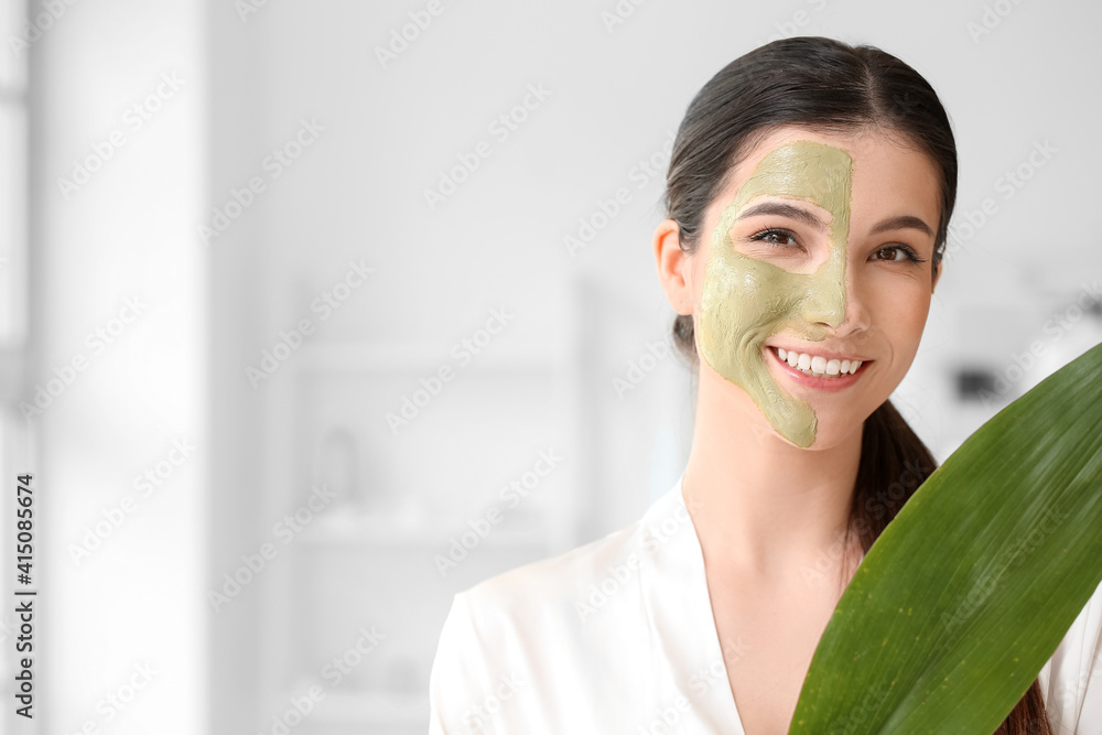 Beautiful young woman with facial mask and tropical leaf in bathroom, closeup