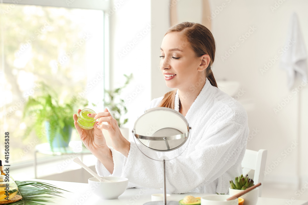 Beautiful young woman applying cosmetic product in bathroom