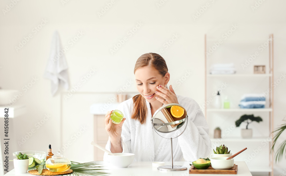 Beautiful young woman applying cosmetic product in bathroom