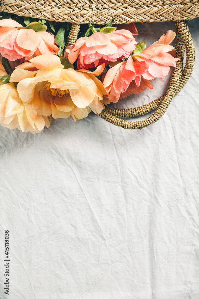 Flat-lay of Beautiful peony flowers in straw bag over grey linen table cloth background