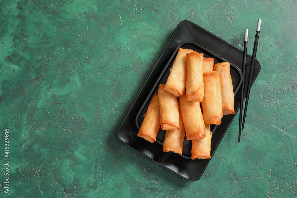 Plate with tasty fried spring rolls on color background