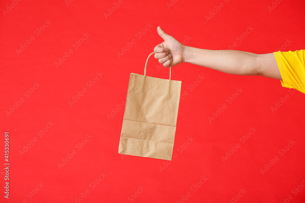 Hand of courier with paper bag on color background