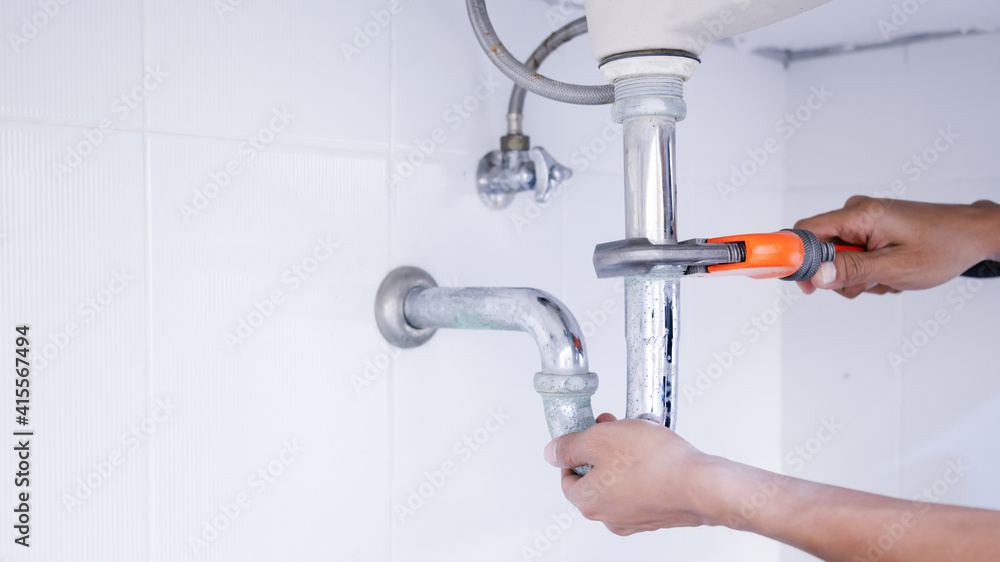 Plumber working in the bathroom, plumbing repair service, repairing leaking sinks with adjustable wr