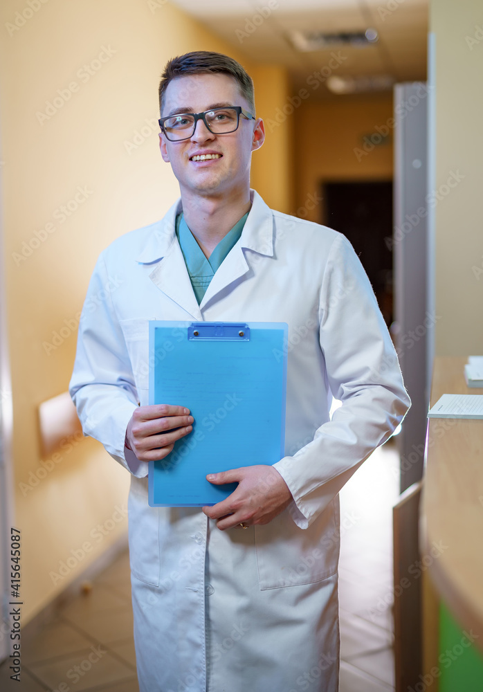 Medic in scrubs holds folder and stands in clinic corridor ready to give consultation. Hospital and 