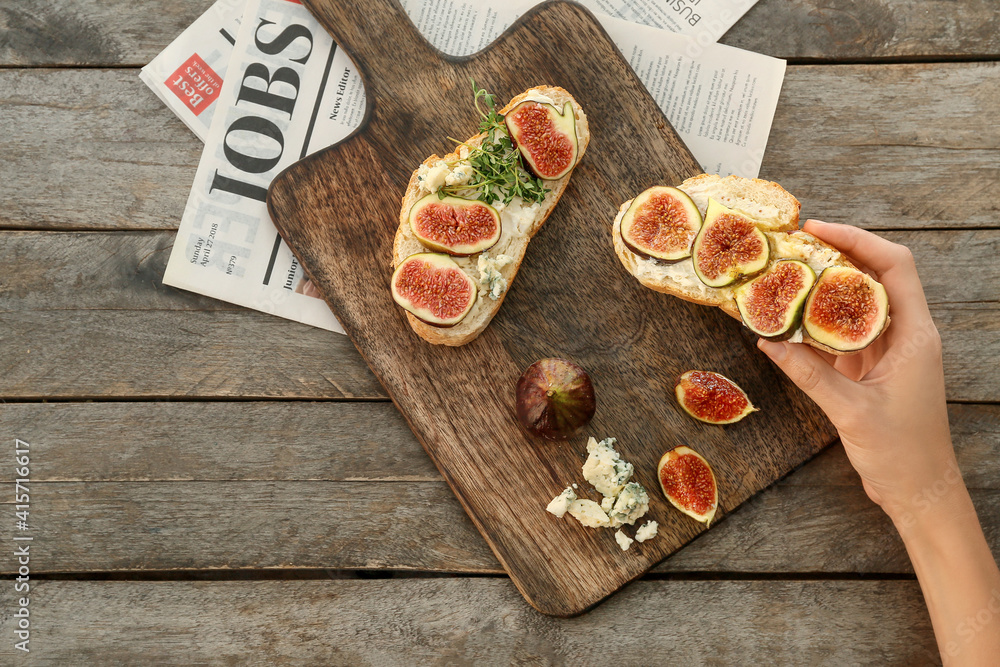 Woman holding tasty sandwiches with fig on wooden background