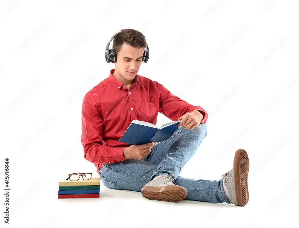 Young man with headphones reading books on white background