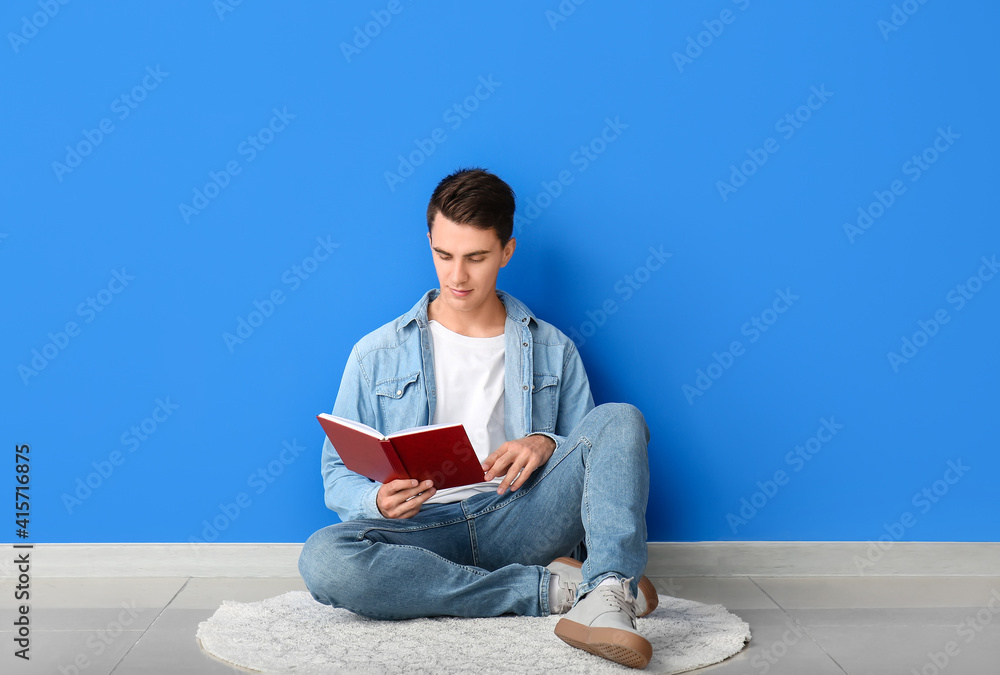 Young man reading book near color wall