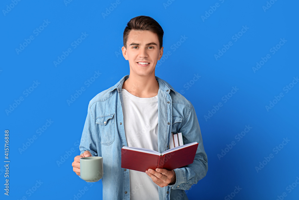 Young man with cup of coffee and book on color background