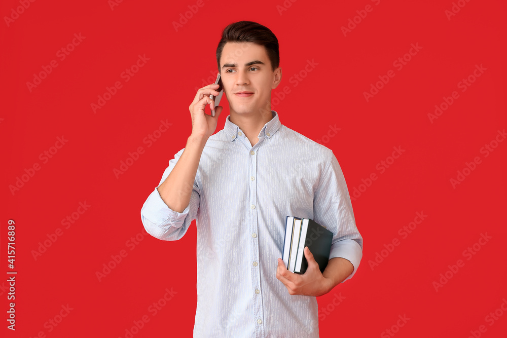 Young man with books talking by mobile phone on color background