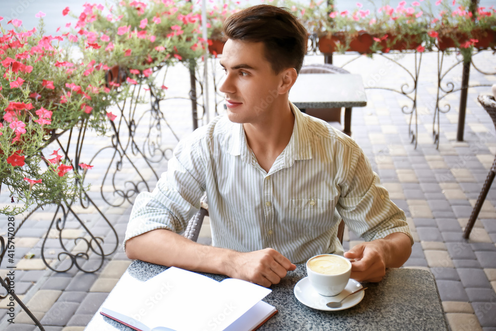 Young man with book drinking coffee in outdoor cafe