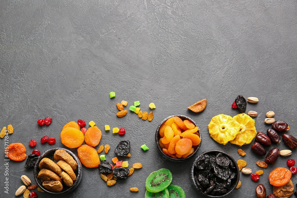 Bowls with different dried fruits on dark background