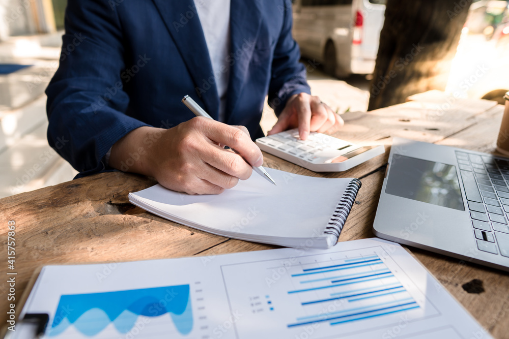 Business accountants are taking notes in notebooks and using a calculator to calculate financial cos