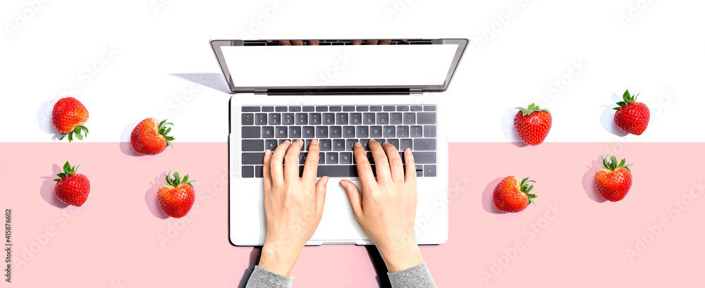 Woman using a laptop computer with fresh strawberries from above