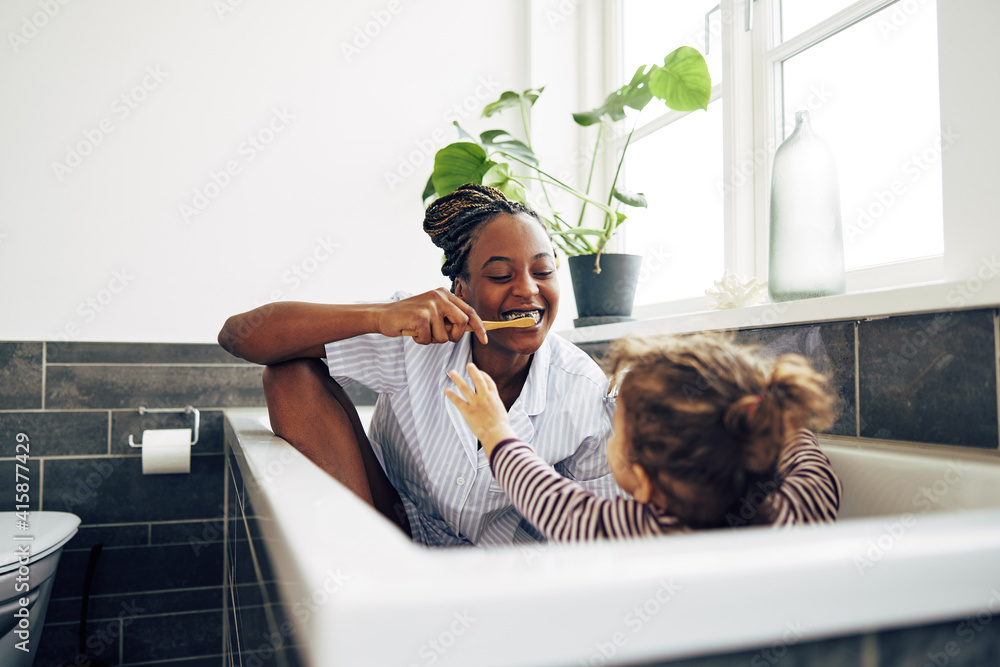 Smiling mom teaching her little girl how to brush her teeth