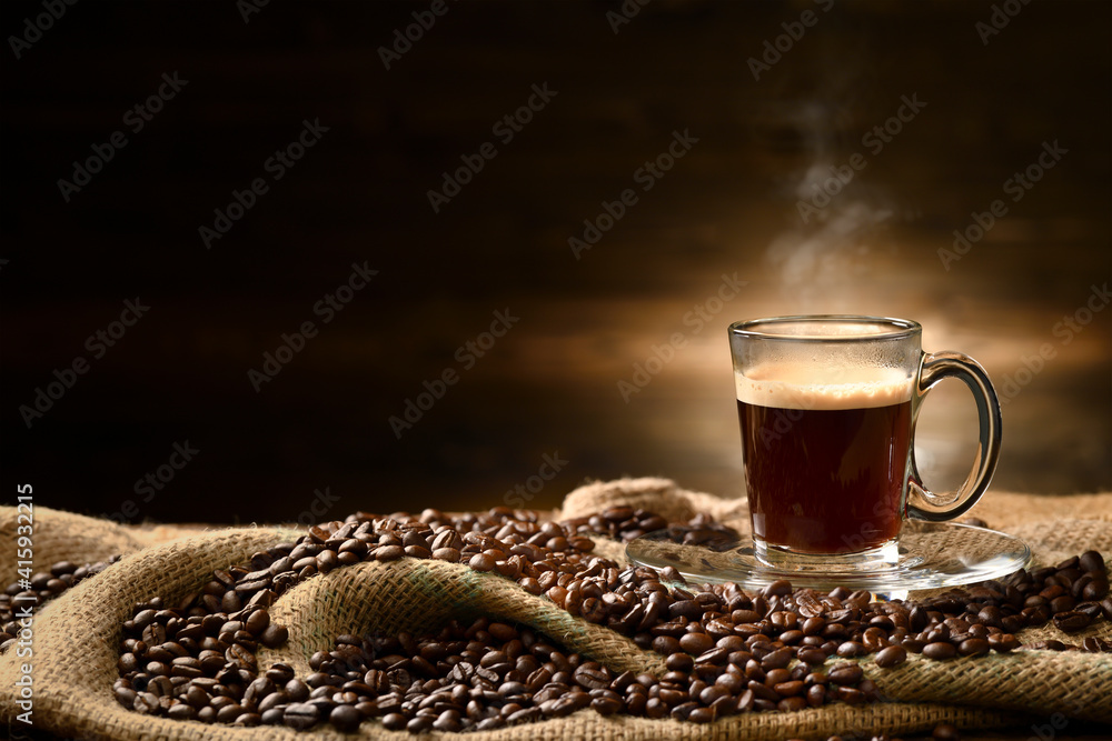 Cup glass of coffee with smoke and coffee beans on burlap sack on old wooden background