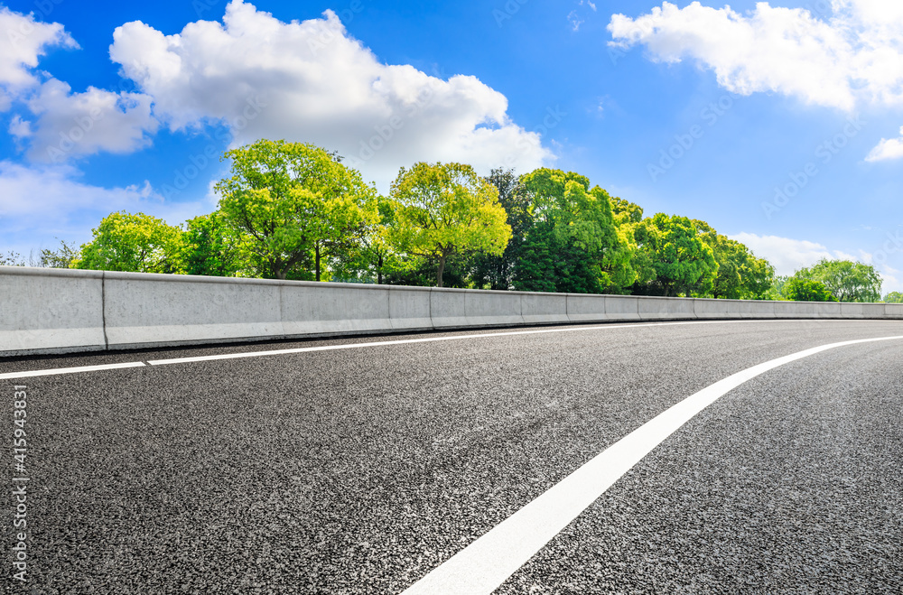 Empty road and green tree under blue sky.