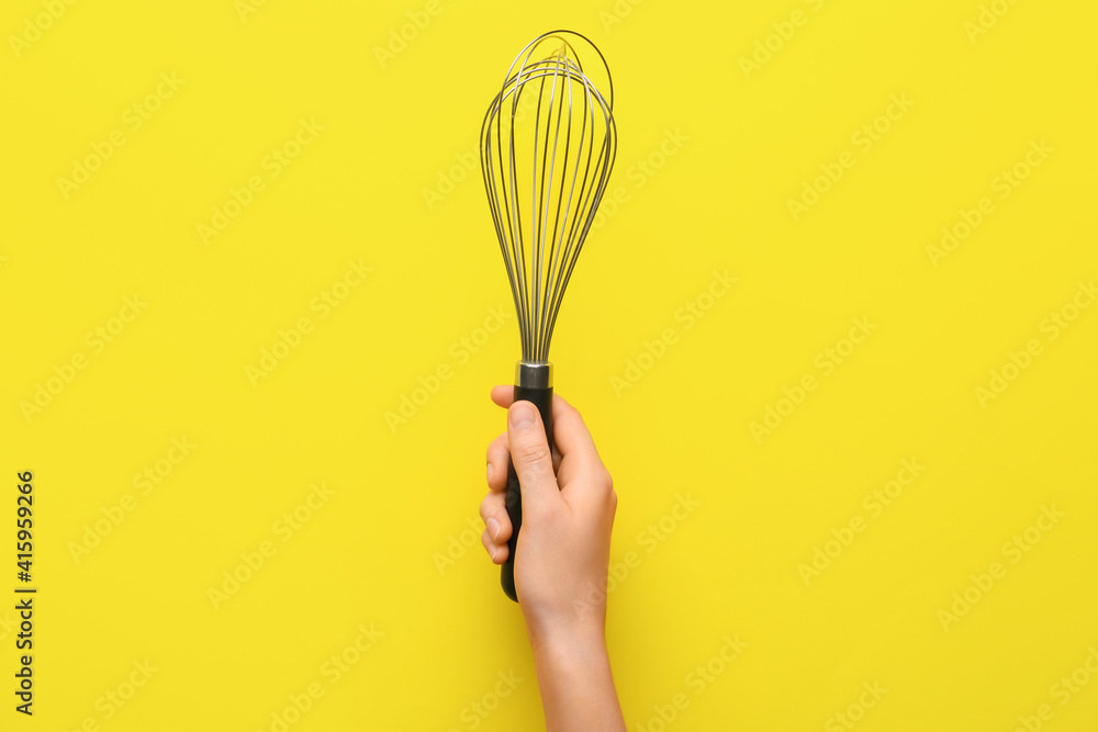 Female hand with whisk on color background